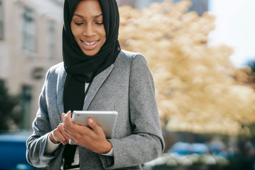 pexels photo 5999904 5999904 Happy crop young African American lady in elegant suit and traditional hijab smiling while browsing tablet on city street