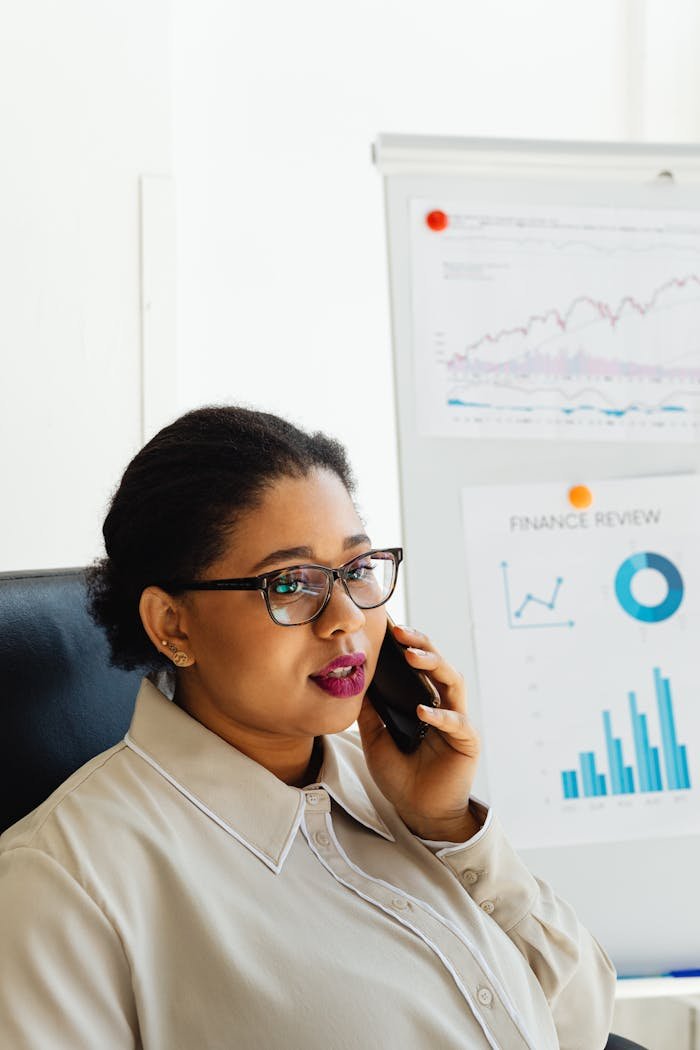 Accueil African American woman in office, analyzing finance charts on white board, talking on phone.